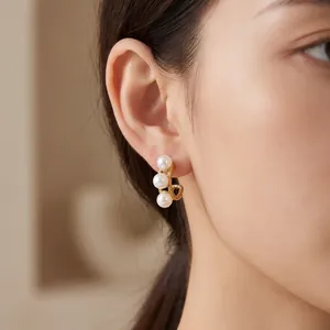 Elegant detailbeeld van drie schelpparels op 18k vergulde C-vormige oorbellen gedragen aan oor