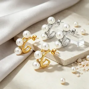 Detailopname van gouden en zilveren C-vormige oorbellen met drie witte parels op steen