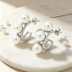 Elegante C-vormige roestvrijstalen oorbellen met drie schelpparels op marmeren basis.