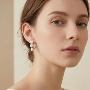 Close-up van een model met elegante C-vormige oorbellen versierd met schelpparels.