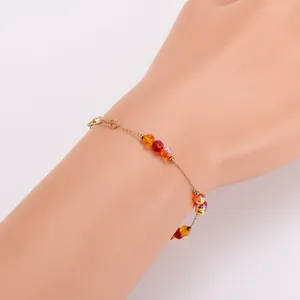 Detailansicht eines vergoldeten Armbands mit bunten irisierenden Perlen am Handgelenk.