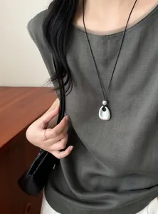 Detail shot of a minimalist matte silver pendant necklace with a black cord on a model