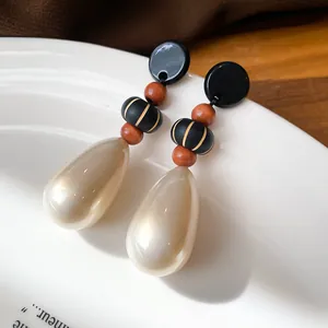 Close-up of vintage style teardrop pearl earrings with wooden beads and black accents.