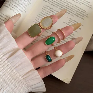 Detailed macro shot of a seven-piece set of gold and green resin rings on a hand.