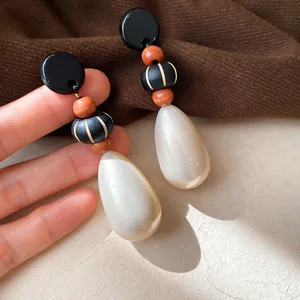 Close-up of vintage style teardrop pearl earrings with wooden beads and black accents