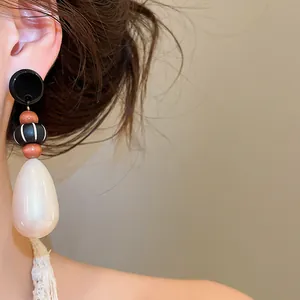 Detail view of vintage waterdrop pearl earrings with wooden beads on model's ear.