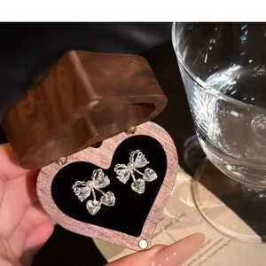 Close-up of delicate zircon pearl bow earrings displayed in a heart-shaped wooden box