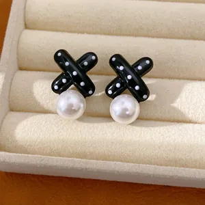 Detailansicht der schwarzen X-förmigen Ohrstecker mit Polka Dots und weißer Perle