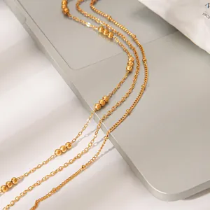 Close-up of three gold-layered necklaces with bead accents on a sleek surface