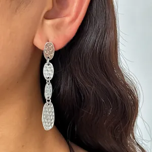 Dettaglio ravvicinato di orecchini pendenti ovali in argento martellato su una modella