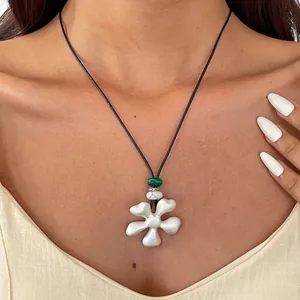 Gros plan d'un collier pendentif fleur blanche de style ethnique sur un cordon en cuir.
