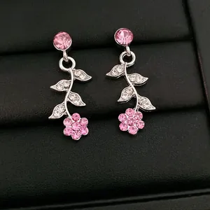 Nahaufnahme von eleganten rosa Blumen- und Blatt-Ohrringen mit Strasssteinen auf Leder.