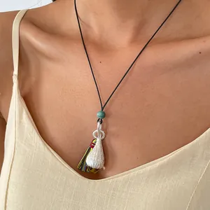 Détail d'un collier pendentif goutte en argent style ethnique avec pompon et cordon cuir.