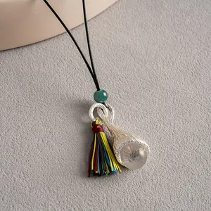 Gros plan d'un pendentif ethnique avec texture argentée, gland coloré et pierre claire