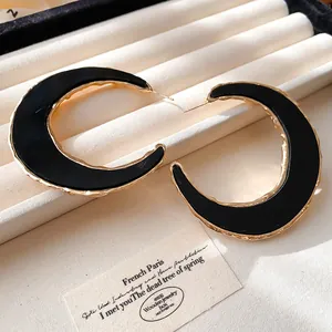 Detailaufnahme der übergroßen C-förmigen Creolen mit schwarzem Inlay und Goldrand.