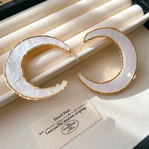 Nahaufnahme übergroßer goldener C-Ohrringe mit weißer Marmor-Acetat-Einlage