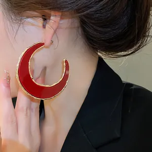 Nahaufnahme eines übergroßen roten C-förmigen Halbmond-Ohrrings mit goldenem Metallrand