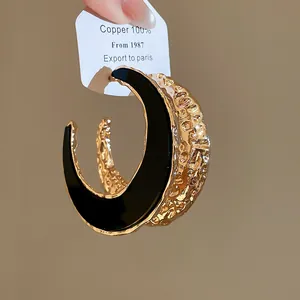 Detailaufnahme von strukturierten, gold-schwarzen C-förmigen Metall-Creolen für Damen