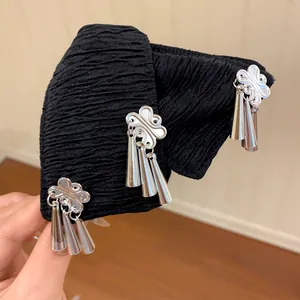 Detailweergave van een zwarte geplooide haarclip met zilveren bloemendecoraties.