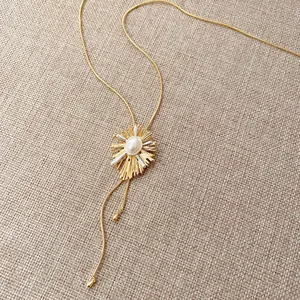Macro detail of the 18k gold plated sunburst pendant featuring a central pearl