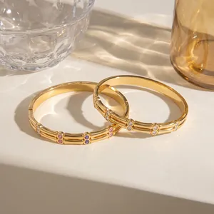 Close-up detail of two gold stainless steel bangles featuring vibrant CZ stone inlays.