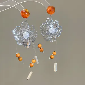 Detailed view of hollow flower earrings with pearl and orange resin bead tassels