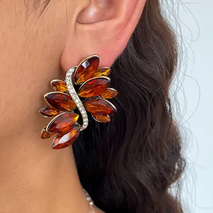 Close-up van amberkleurige glazen bladvormige oorknopjes met fonkelende strass-steentjes.