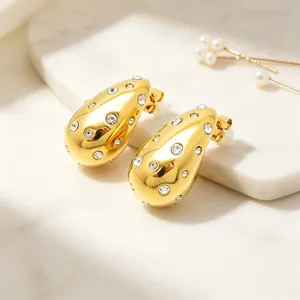 Detailed view of gold teardrop earrings with embedded crystals on marble background.