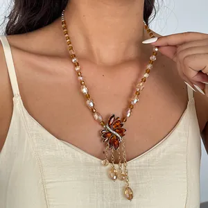 Detail van amberkleurige glazen kralenketting met blad hanger van strass en kwastjes