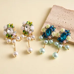 Macro di eleganti orecchini decorati con fiori di resina, cristalli e nappine di perle.