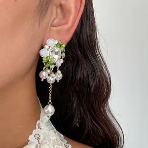 Dettaglio di orecchini a fiore con strass e nappe di perle indossati da una modella