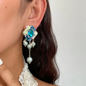 Dettaglio di orecchini con gemma blu, nappe di perle e fiori in resina in stile barocco