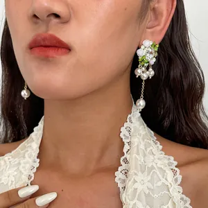 Dettaglio di orecchini lunghi con nappe di perle, fiori in resina e strass su modella.