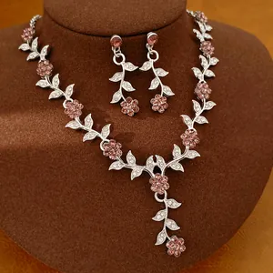Elegant silver jewelry set featuring pink crystal flowers and leaves on a brown display