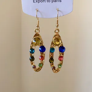 Vue macro de boucles d'oreilles ovales dorées avec strass multicolores et finition martelée