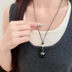 Primo piano di una collana con orsetto nero in resina e fiocco bianco su cordino