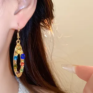 Vue détaillée de boucles d'oreilles ovales dorées avec strass multicolores à l'oreille