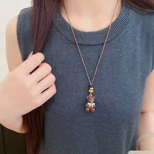 Primo piano di una collana con ciondolo a forma di orso marrone indossata su un top grigio.