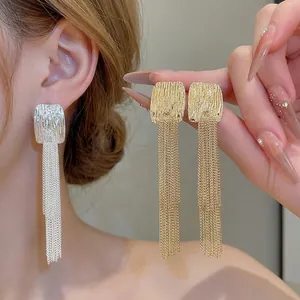 Elegant long gold and silver tassel earrings with pleated metal texture on model's ear.