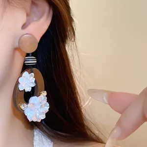 Nahaufnahme von Vintage-Holzohrringen mit zarten weißen Muschelblumen, von Modell getragen
