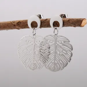 Detailed macro shot of silver hollow monstera leaf earrings on a natural wooden branch