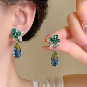 Nahaufnahme eleganter Tropfenohrringe mit grünen Steinen und blauem Farbverlauf.