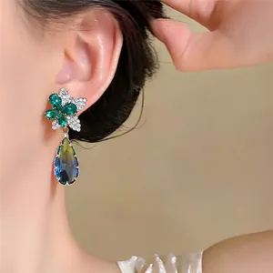 Detail der silbernen Ohrstecker mit grüner Kristallblume und blauem Tropfenanhänger.