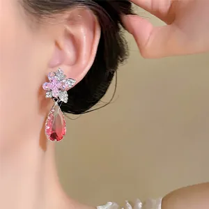 Nahaufnahme von rosafarbenen Blumenohrringen mit rotem Tropfenanhänger an einem Model.