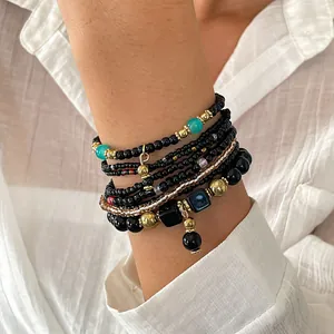 Detailopname van een acht-delige zwarte en gouden glazen kralenarmbandset om de pols