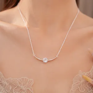 Close-up of a delicate silver necklace with a curved bar and round zircon pendant.