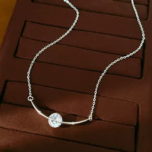 Close-up of silver-tone curved necklace with round clear zircon on brown velvet tray.