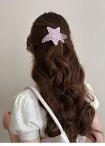 Close-up detail of a pink star acetate hair clip with polka dots on long wavy brown hair