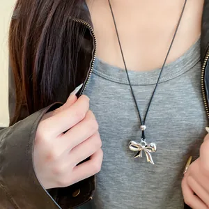Detalle de un colgante de lazo de plata pulida en un collar minimalista de cordón de cuero.