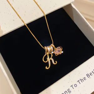 Gros plan du collier plaqué or orné d'un pendentif lettre R et d'un charm en zircon rose